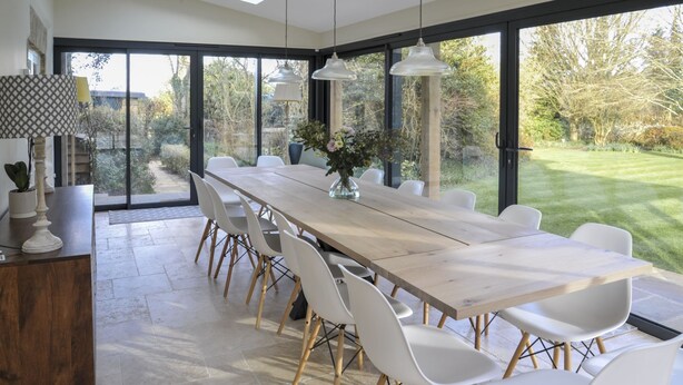 A modern dining area with a long table, white chairs, and a vase of flowers.
