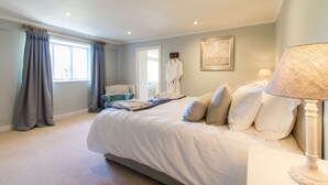 A bedroom with a large bed, a bedside table with a lamp, a chair, and a window with curtains.