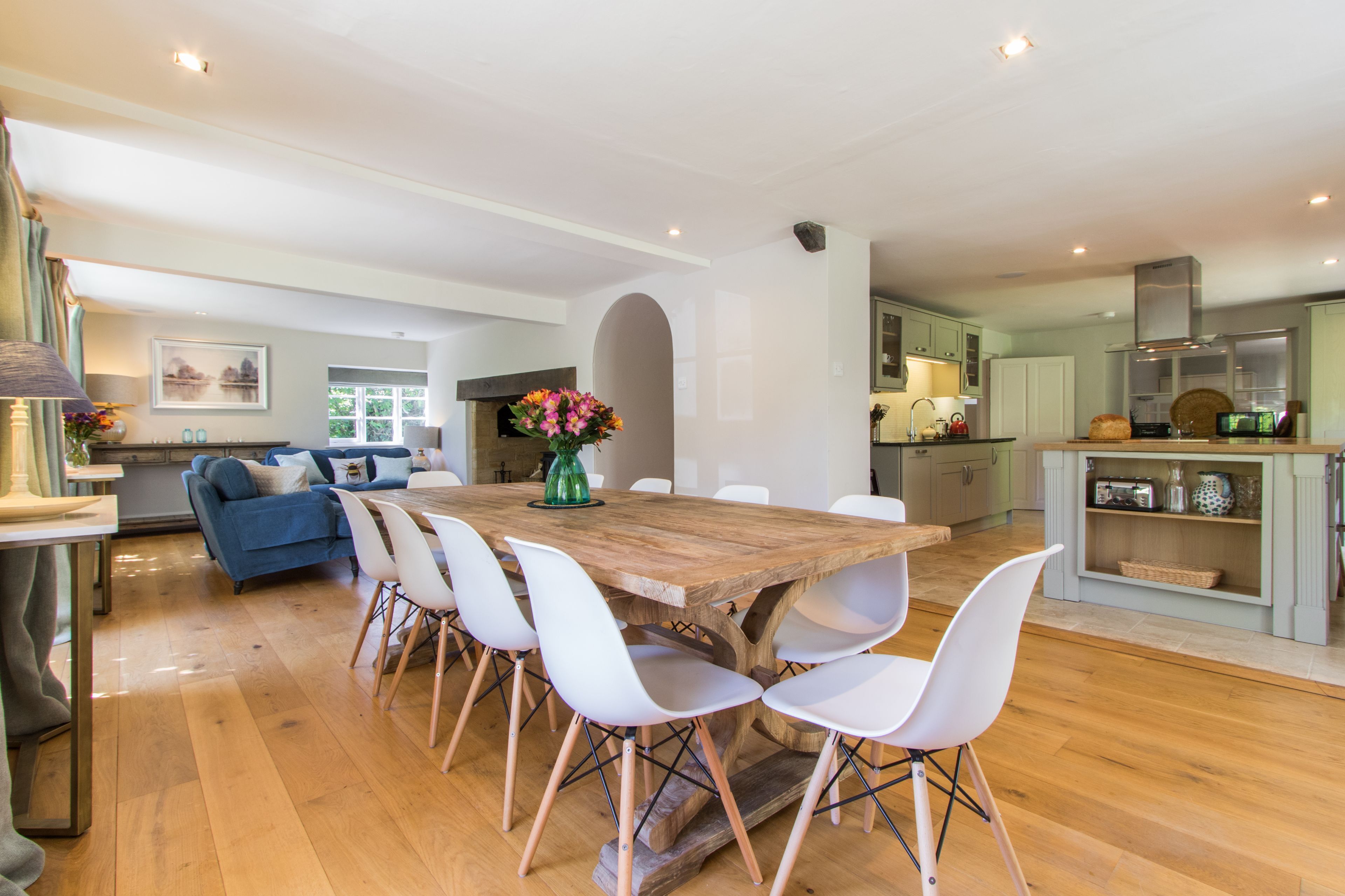 A spacious living area with a wooden dining table surrounded by white chairs, a blue sofa, and a fireplace.
