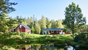 A red barn and a modern house with solar panels, surrounded by lush greenery and a calm pond. - "Slamrekullen" our place in Ullared - Sweden (Ullared)