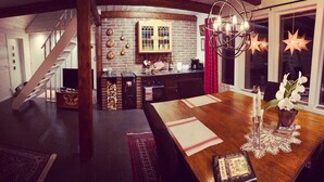 Un comedor acogedor con una mesa de madera, una araña y vistas a una cocina con paredes de ladrillo y una escalera.