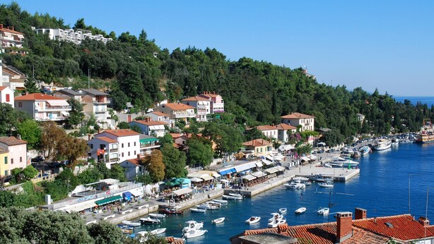 A coastal town with a marina, houses with red roofs, and a clear blue sea.