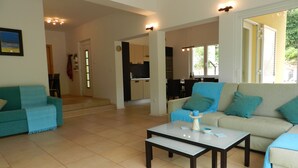 A spacious living area with a sofa set, a coffee table, and a kitchen in the background.