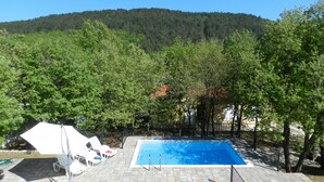 A swimming pool surrounded by trees, with a hilly landscape in the background.