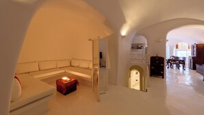 A spacious living area with a white sofa, a small red ottoman, and a dining area with wooden furniture.