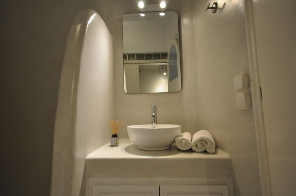 A bathroom with a white sink, a mirror, and two rolled towels on the counter.