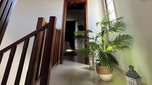 Eine Treppe mit hölzernen Geländern führt zu einer Zwischenebene. Auf der Zwischenebene befinden sich ein Blumentopf und ein Laternen.