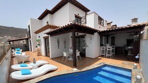 Ein modernes Haus mit Schwimmbad, Außenbereich mit Sitzgelegenheit und Küchenzeile.