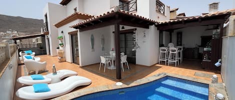 Ein modernes Haus mit Schwimmbad, Außenbereich mit Sitzgelegenheit und Küchenzeile.