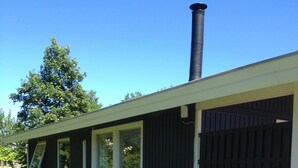 Ein modernes Gebäude mit schwarzer Fassade, einem Schornstein und einer überdachten Außenbereich mit Sitzbank.