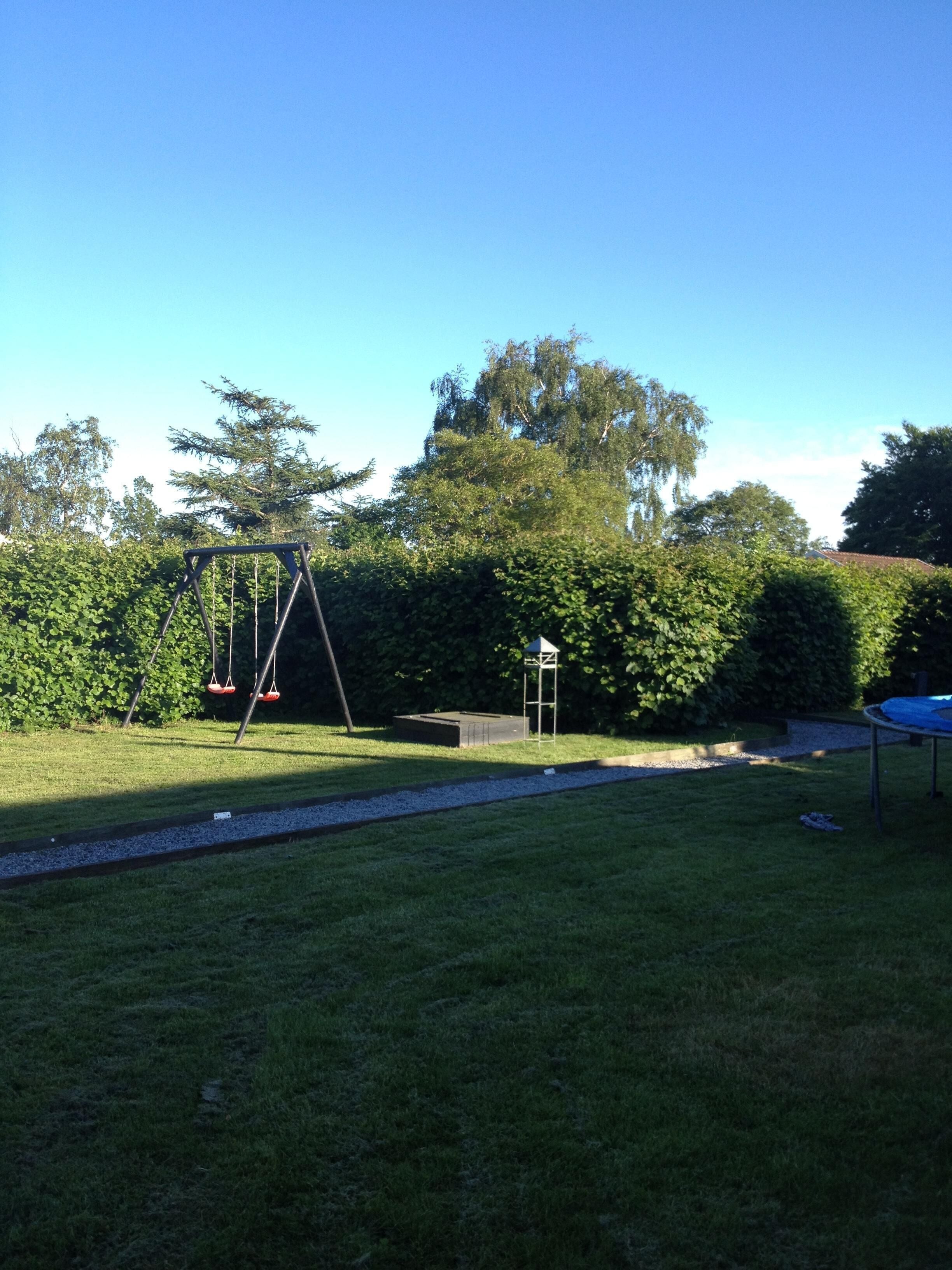 A grassy backyard with a swing set, a small gazebo, and a trampoline.