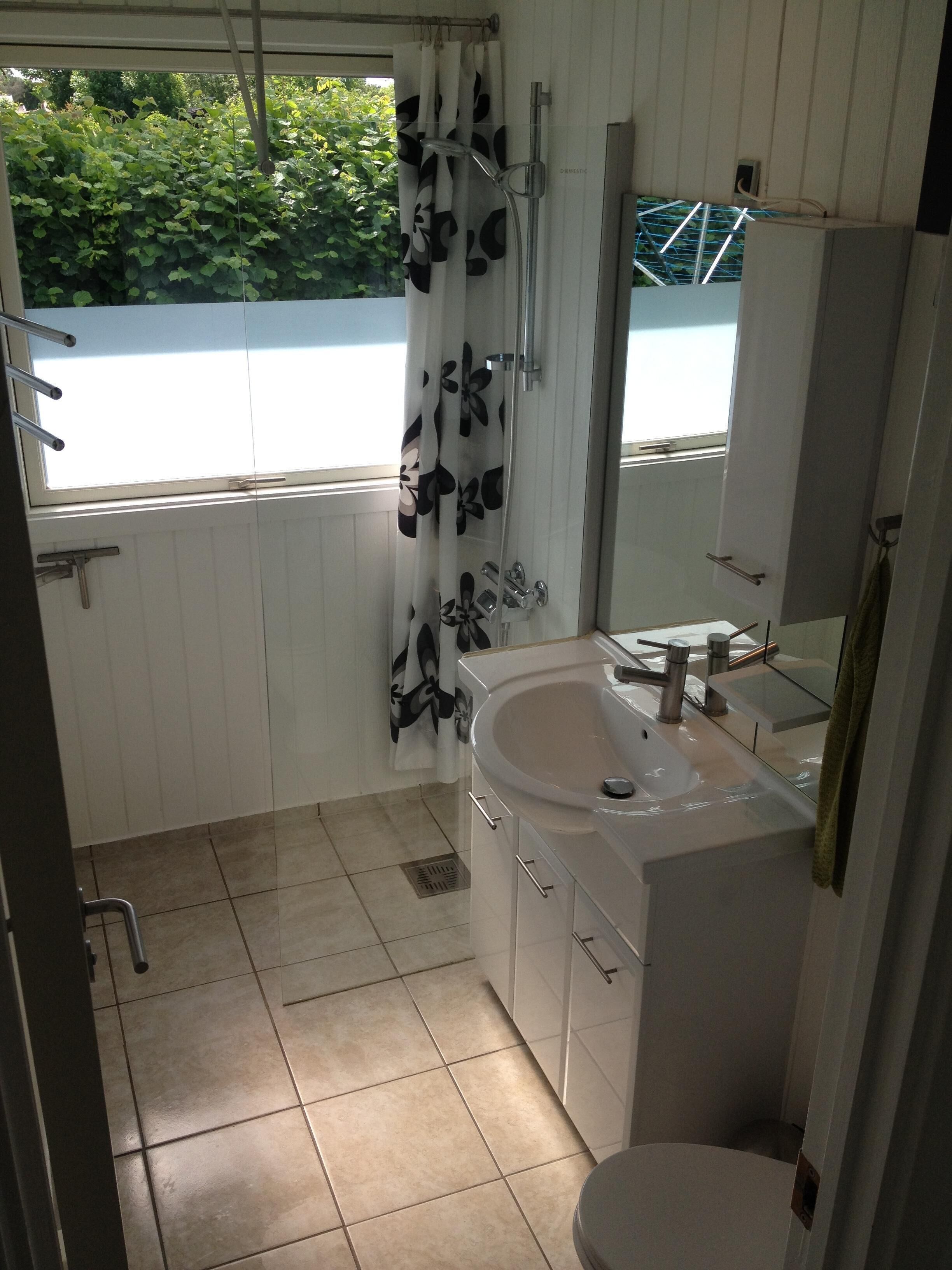 A bathroom with a shower, toilet, sink, and a window with a view of greenery.