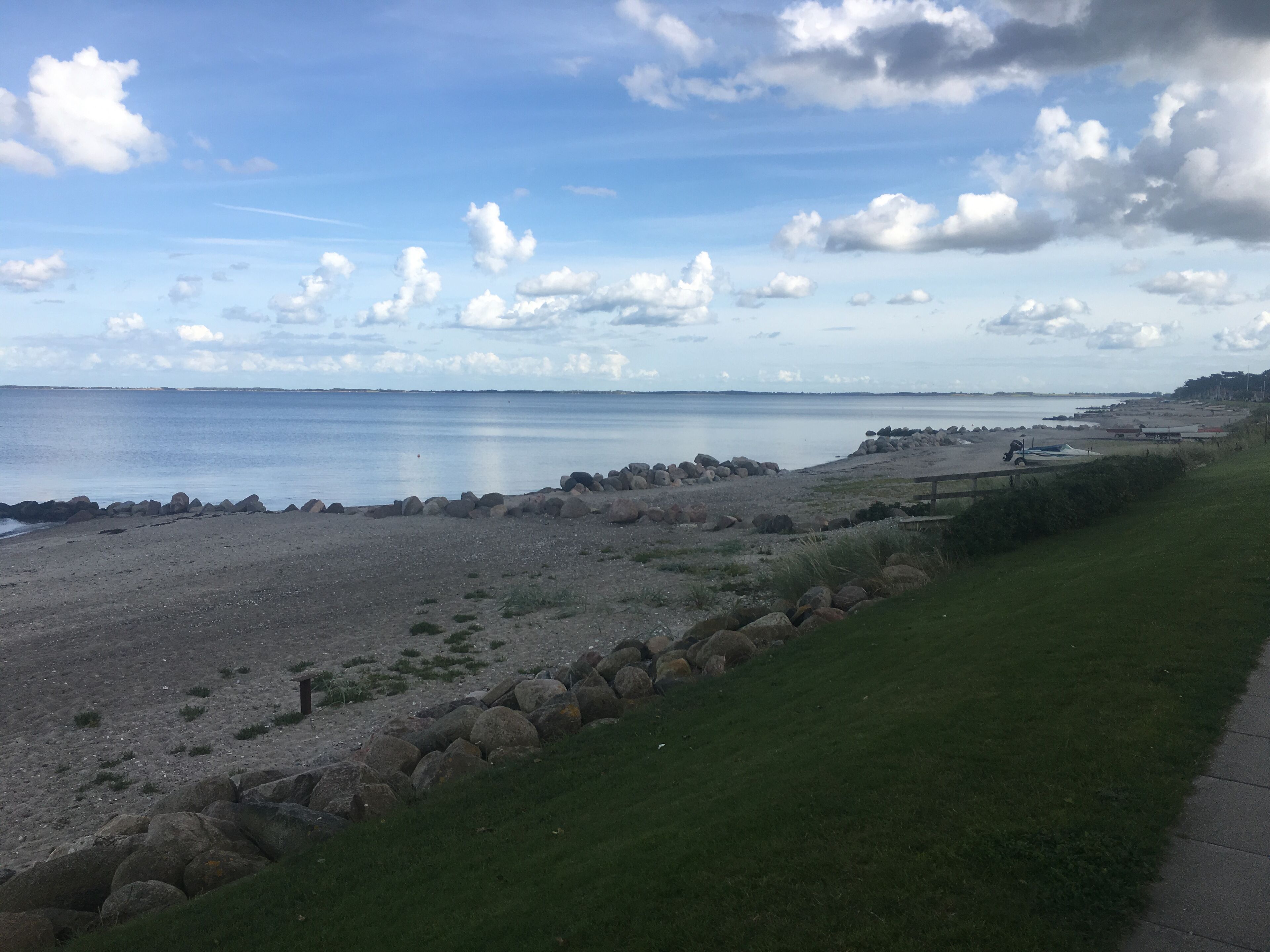 Paesaggio costiero con spiaggia rocciosa, area verde e vista libera sul mare e cielo.