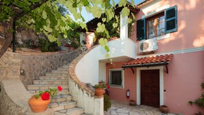 A stone staircase leading to a pink building with a tiled roof, a wooden door, and potted plants. - Vill Pergola Elli, holiday apartment in Corfu, Greece with stunning sea view! (Corfu)