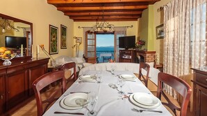 A dining area with a table set for six, wooden chairs, a television, and a view of the sea. - Vill Pergola Elli, holiday apartment in Corfu, Greece with stunning sea view! (Corfu)