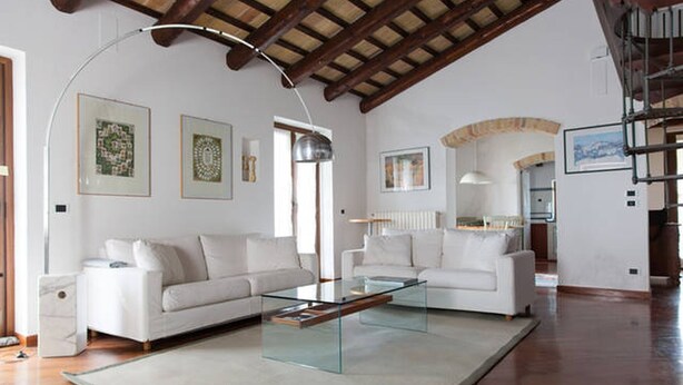 Un soggiorno spazioso con due divani bianchi, un tavolino in vetro e un soffitto alto con travi a vista in legno.