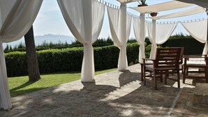 Un’area salotto esterna coperta, con pavimento in pietra e tende bianche.
