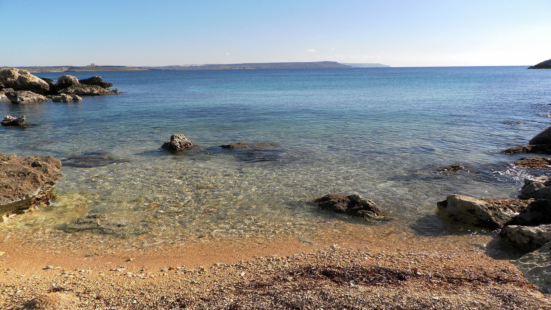 Una playa rocosa con agua cristalina y tierra a lo lejos.