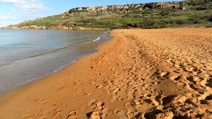 A sandy beach with footprints, a calm sea, and a rocky hillside in the background. - Great Location: FREE Gozo transfers, WIFI, Bicycles & BBQ  – NO Car required! (Ghajnsielem)