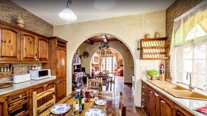 A kitchen with wooden cabinets, a dining area with a table set for four, and an archway leading to another room. - Great Location: FREE Gozo transfers, WIFI, Bicycles & BBQ  – NO Car required! (Ghajnsielem)
