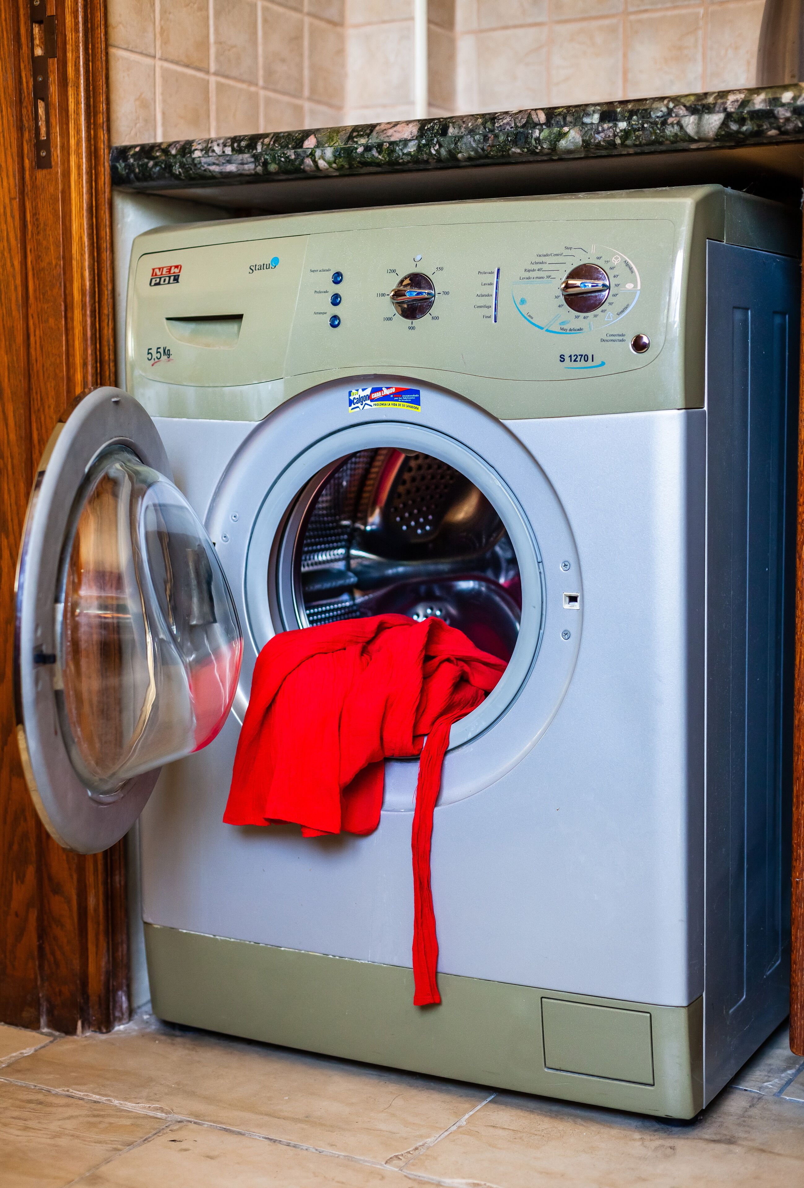 Een wasmachine met voorlader, met een rode handdoek aan de deur.