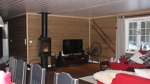 A cozy living room with a wooden interior, a fireplace, a television, and a red sofa. - Luxury cottage with panoramic views. Proximity to summer and winter activities. (Hemsedal)
