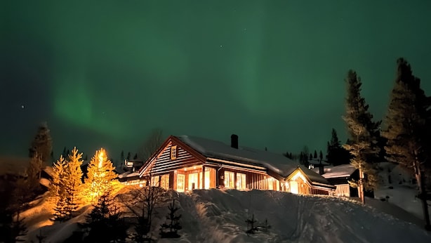A snow-covered landscape with a wooden cabin illuminated by warm lights, surrounded by snow-covered trees and a clear night sky. - Luxury cottage with panoramic views. Proximity to summer and winter activities. (Hemsedal)