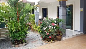 A well-maintained garden with various plants and flowers in front of a building with a white facade and grey pillars. - ⭐⭐⭐⭐⭐Villa 4 bedrooms with private pool 5 minutes beaches and Walking Street. (pattaya)