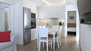 A compact kitchen with white cabinets, a built-in oven, and a refrigerator. There is a dining area with a white table and chairs.