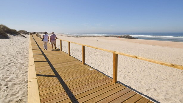 A wooden boardwalk along a sandy beach with a clear sky.