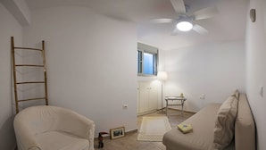 Ein kleiner, gut beleuchteter Raum mit Deckenventilator, Fenster, Lampe, kleinem Tisch und zwei Sofas.