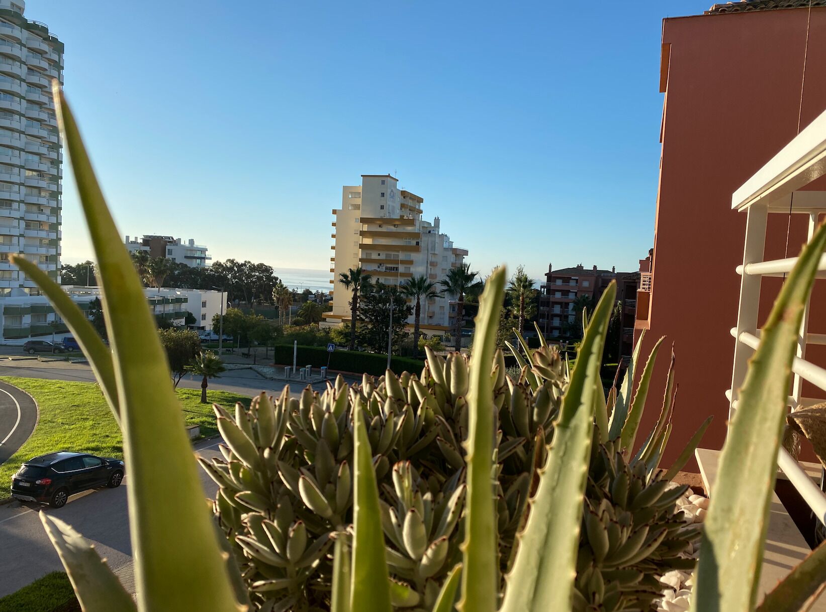 A residential area with a building featuring balconies and a clear view of the sea.