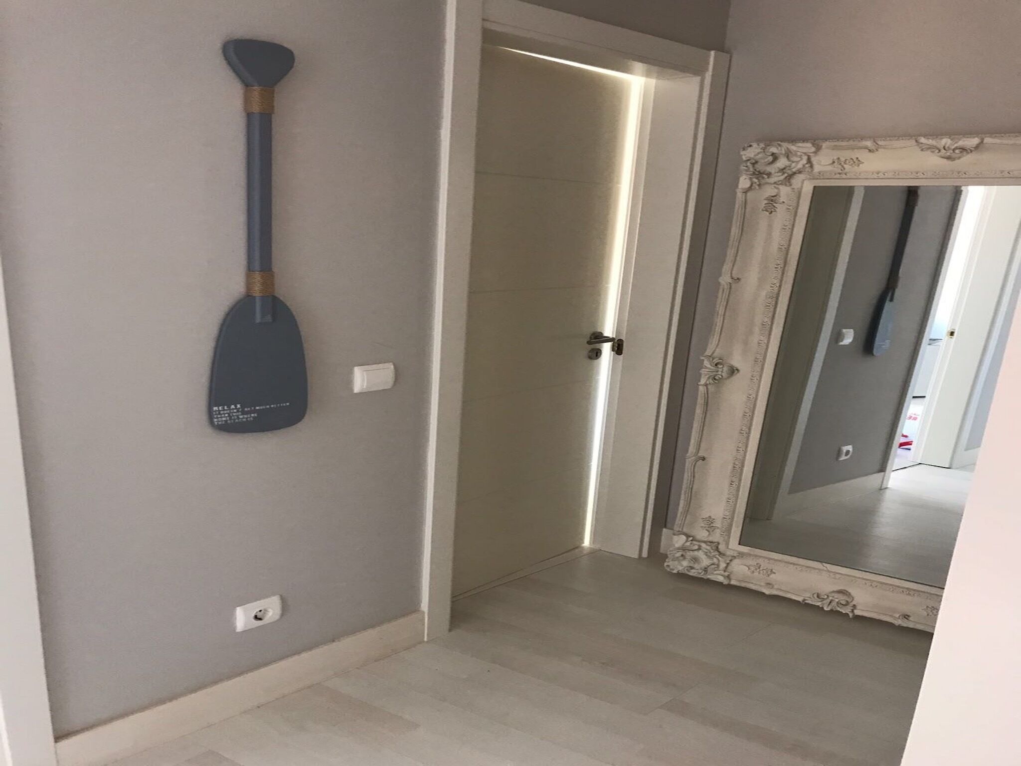 Un corridoio con una parete grigia, una pagaia blu, una porta bianca e uno specchio con cornice decorata.