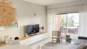 A modern living room with a flat-screen TV, a dining table, and a sofa. - Saltwater Apartment - Sea View (Portimão)