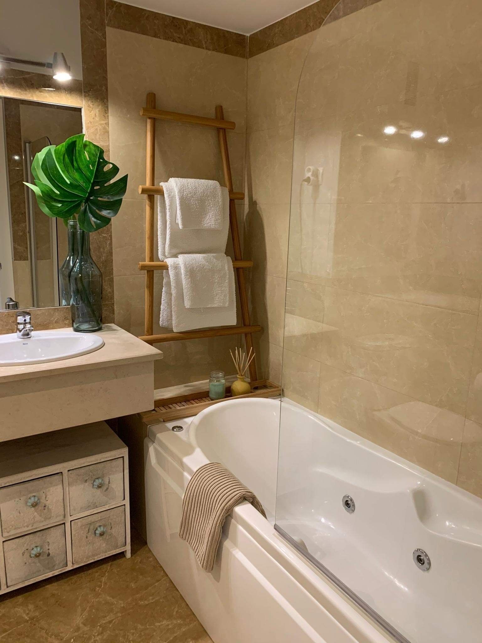 Une salle de bain avec une baignoire, une échelle en bois, un miroir, un lavabo et une plante.