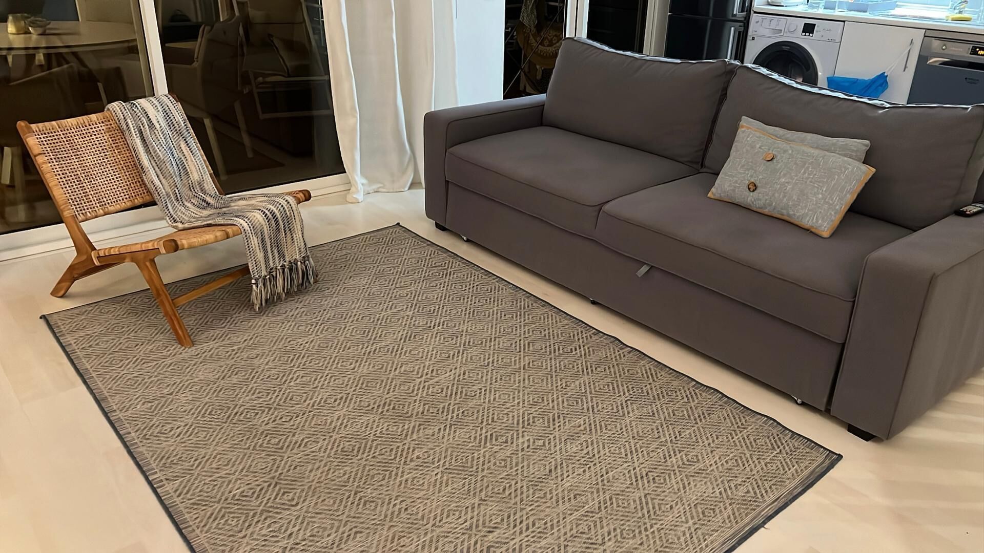 Una sala de estar con un sofá gris, un tapete estampado y una silla de madera con una manta.