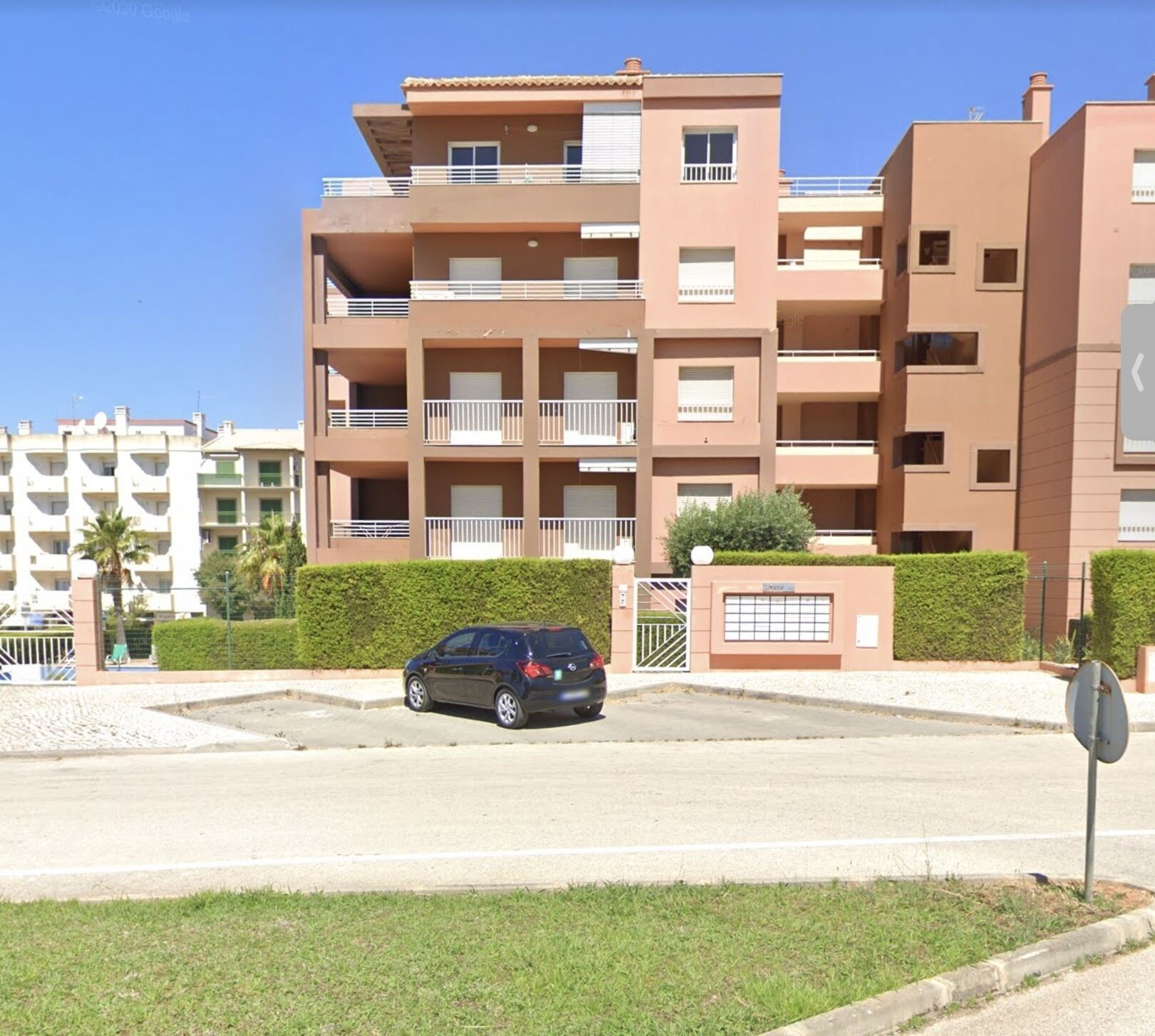 Un edificio residencial de varios pisos con balcones, acceso mediante portón y zona de estacionamiento.