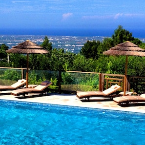 Un espace aménagé au bord de la piscine, avec des chaises longues et des parasols en chaume, offrant une vue sur le paysage urbain.