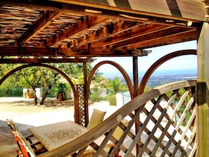 Une pergola en bois, agrémentée d’un hamac et d’une table, offre une vue imprenable sur un paysage pittoresque, avec des arbres et une vue lointaine sur l’océan.
