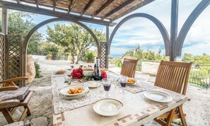 Un espace de restauration en plein air avec une table dressée pour deux personnes, entourée de chaises en bois et d’une structure en forme de pergola.