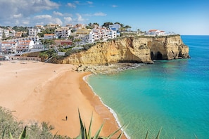A coastal town with buildings on a cliff overlooking a sandy beach and turquoise waters.