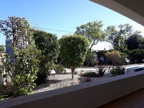 A balcony with a view of a garden, including various trees and a building in the background.