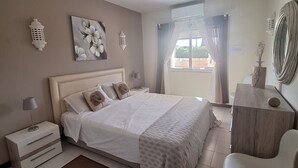 Ein Schlafzimmer mit Bett, Nachttischen, einem Sessel, einem Schreibtisch und Wanddekoration.