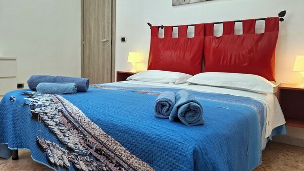 A neatly made bed with blue bedding, a red curtain, and a wall-mounted painting. - HOLIDAY HOME Central Station, Business Center, Naples city center, Mary's Room (Napoli)