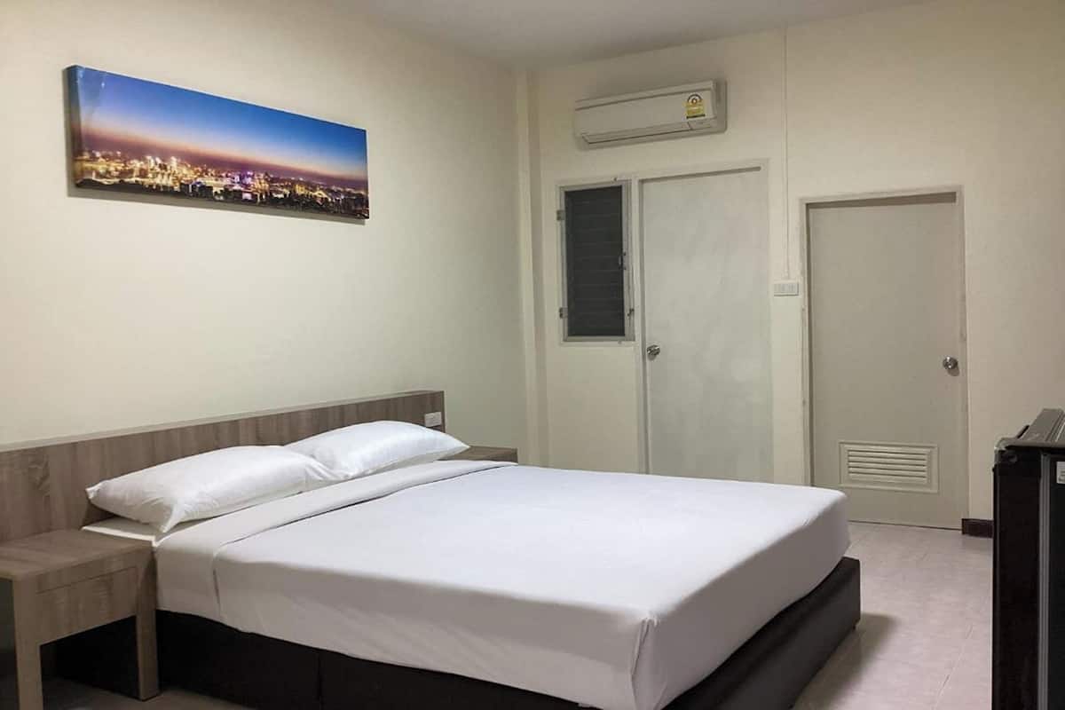 A hotel room with a bed, a nightstand, a wall-mounted air conditioner, and a door.