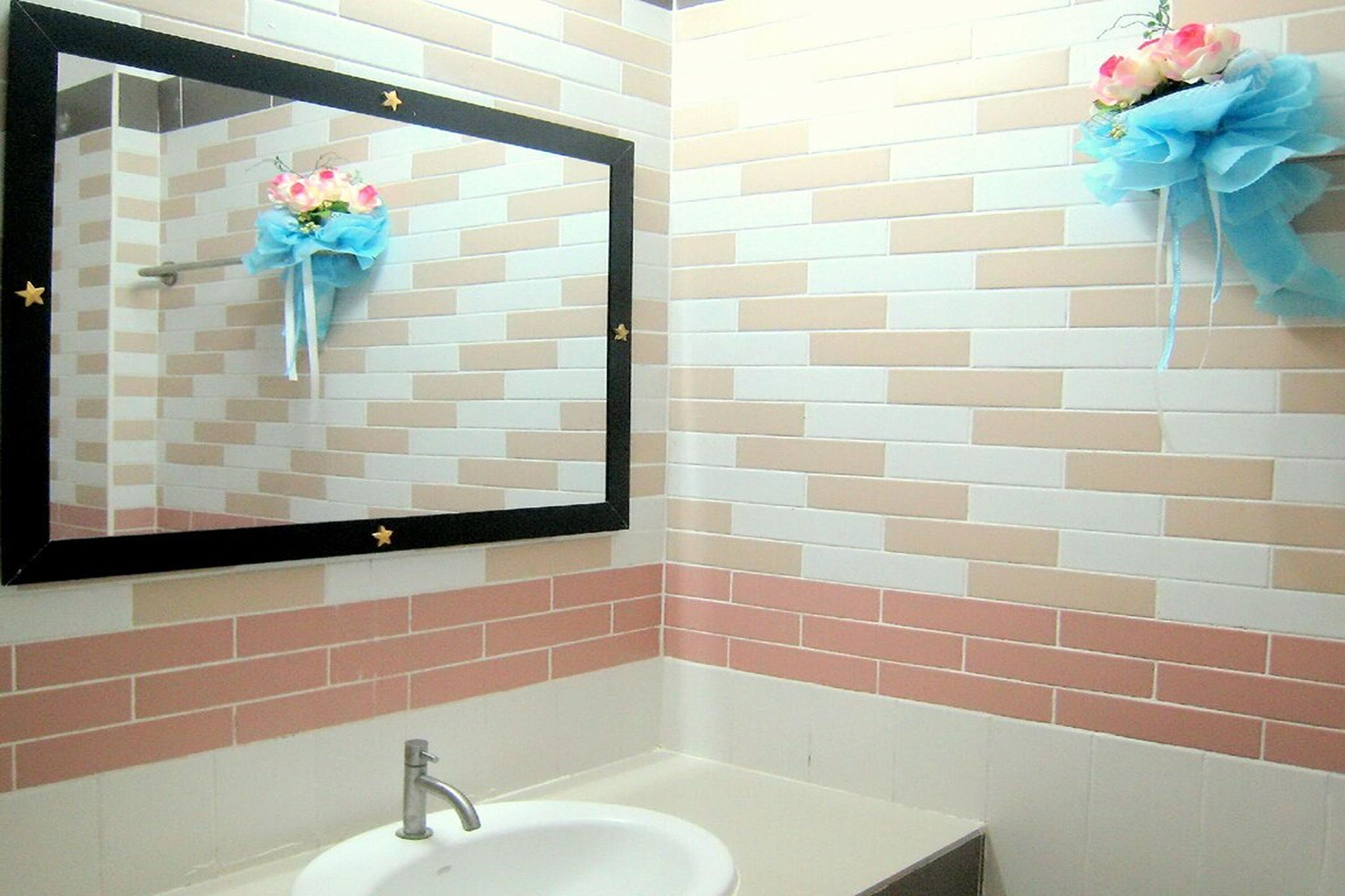 A bathroom with a white sink, a mirror with a black frame, and pink and beige tiles.