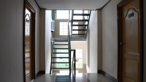Un couloir avec un escalier menant à l’étage supérieur, une porte avec une plaque indiquant le numéro, et une fenêtre laissant entrer la lumière naturelle.