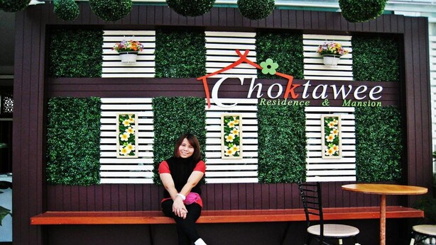 Une femme est assise sur un banc devant un mur sur lequel on peut lire l’inscription « Choktawee Residence & Mansion ».