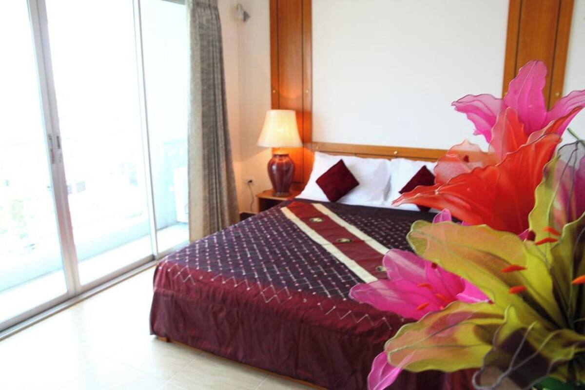 A hotel room with a large bed, a nightstand, a lamp, and a view of the outside.