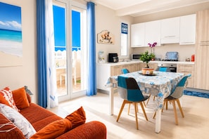 A modern living room with a sofa, a dining area with a table, and a kitchen with cabinets and appliances.